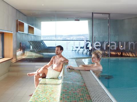 Mann und Frau im Ruhebereich der Sauna, Frau im Warmwasserbecken, Mann sitzt davor auf einem Absatz.